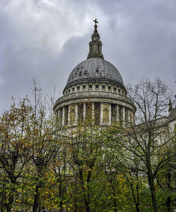 London United Kingdom 15 November 2025 View of St Pauls Cathedral dome framed by autumn trees under a cloudy sky.
