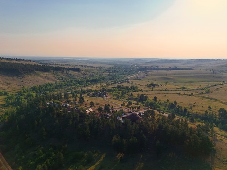 Aerial view of the landscape surrounding Eldorado Springs featuring dense pine forests winding roads and rolling hills under soft golden hour light in Eldorado Springs Colorado United States.
