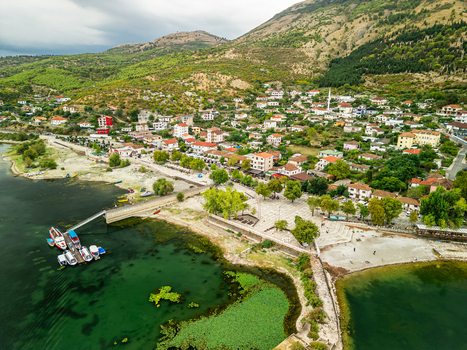 Aerial view of Shiroka village on the shores of Lake Shkodra with boats at a pier stone promenade and lush mountains in Shiroka Shkoder County Albania.
