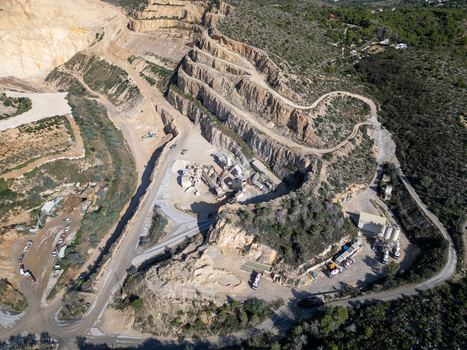 Aerial view of a large open pit stone quarry with terraced rock faces mining machinery and access roads surrounded by Mediterranean vegetation in Teulada Valencian Community Spain.