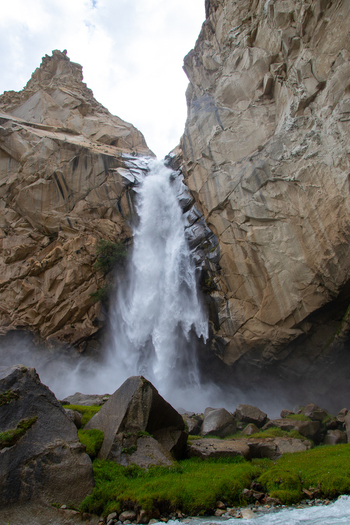 View of Khamosh Waterfall cascading down steep rocky cliffs with green grass and boulders in Skardu Gilgit Pakistan.