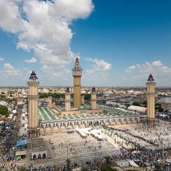 Aerial view of the Great Mosque of Touba featuring its tall minarets and a crowded courtyard under a blue sky with white clouds in Touba Diourbel Region Senegal.