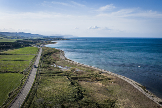 Aerial view of a coastal road winding along the shoreline with green fields and the blue sea in Wakkanai Hokkaido Japan.