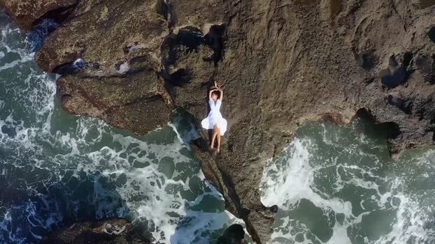 Aerial view of a woman in a white dress on volcanic rocks by the sea Indonesia. Aerial view of a woman in a white dress on volcanic rocks by the sea Indonesia.