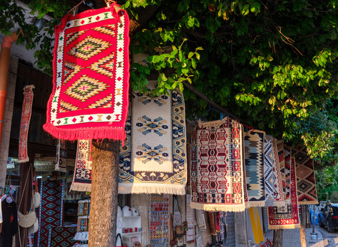 View of traditional colorful handmade rugs and carpets hanging for sale in the old bazaar street under green trees in Kruje Durres County Albania.