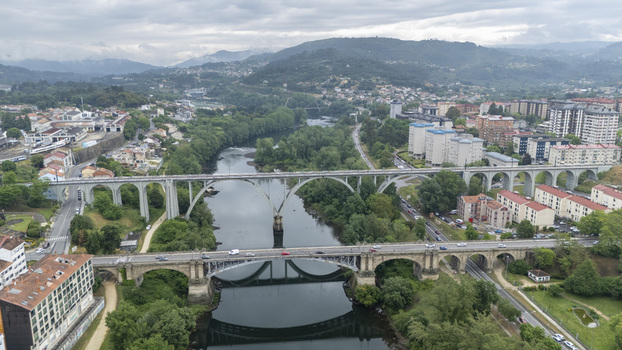 Aerial view of the Ponte Nova bridge and railway viaduct crossing the Minho River surrounded by lush green trees and urban buildings in Orense Ourense Spain.