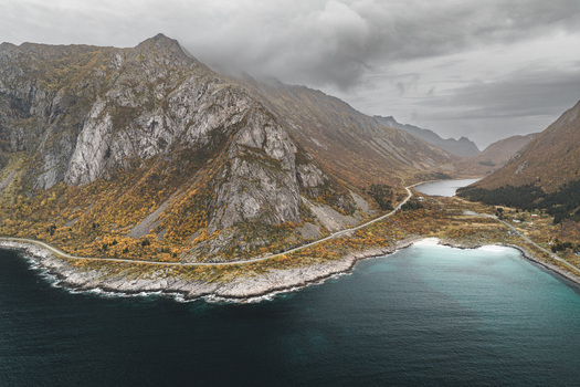Aerial view of the dramatic Lofoten mountains with autumn foliage a winding coastal road and turquoise waters Svolvaer Nordland Norway.