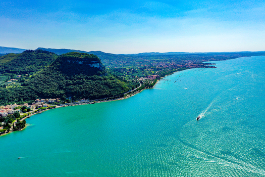 Aerial view of Lake Garda with turquoise water a boat leaving a wake and the lush green Rocca di Garda hill along the coastline Italy. Aerial view of Lake Garda with turquoise water a boat leaving a wake and the lush green Rocca di Garda hill along the coastline Italy.