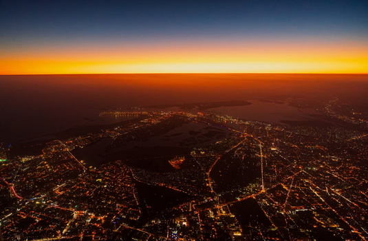 Aerial view of the sprawling cityscape of Karachi at night with glowing street lights and urban infrastructure illuminated under a vibrant sunset sky in Karachi Sindh Pakistan.