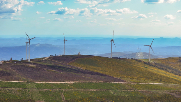 Aerial view of wind turbines on rolling hills with green and brown vegetation a dirt road and a blue sky in Lisbon Lisbon Portugal. Aerial view of wind turbines on rolling hills with green and brown vegetation a dirt road and a blue sky in Lisbon Lisbon Portugal.