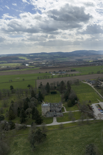 Aerial view of Drum Castle featuring its historic stone tower lush green estate and rolling Scottish countryside under a dramatic cloudy sky Drumoak Scotland United Kingdom.
