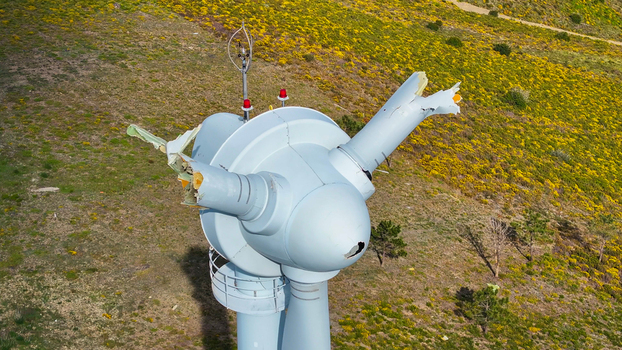 Aerial view of a damaged wind turbine with broken blades and structural damage set against a vibrant yellow flowering hillside in Lisbon Lisbon Portugal. Aerial view of a damaged wind turbine with broken blades and structural damage set against a vibrant yellow flowering hillside in Lisbon Lisbon Portugal.