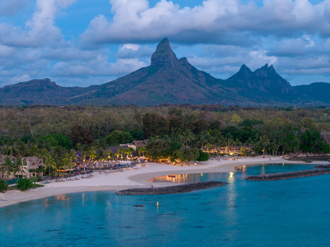 Aerial view of a luxury beach resort at dusk with illuminated villas white sand and the jagged peaks of Rempart Mountain in Moka District Mauritius. Aerial view of a luxury beach resort at dusk with illuminated villas white sand and the jagged peaks of Rempart Mountain in Moka District Mauritius.