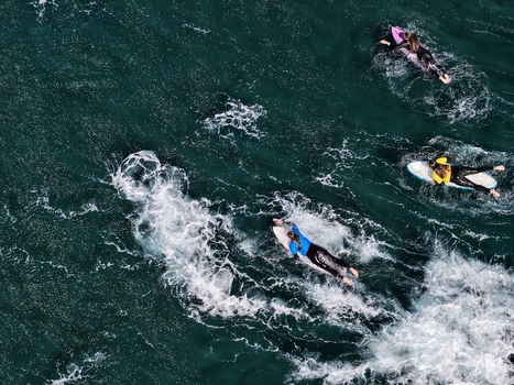 Aerial view of surfers paddling on their boards in the deep blue Atlantic waters off Praia do Areal de Santa Barbara in Ribeira Grande Acores Portugal. Aerial view of surfers paddling on their boards in the deep blue Atlantic waters off Praia do Areal de Santa Barbara in Ribeira Grande Acores Portugal.