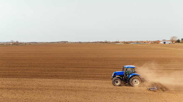 Aerial view of a blue tractor kicking up dust as it tills the vast brown fields under a pale sky Sremska Mitrovica Vojvodina Serbia. Aerial view of a blue tractor kicking up dust as it tills the vast brown fields under a pale sky Sremska Mitrovica Vojvodina Serbia.