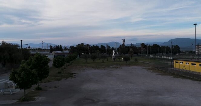 Aerial view of a park with a statue and mountains in Italy.