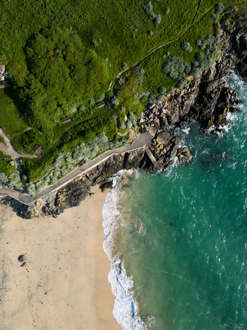 Aerial view of Porthgwidden Beach featuring a sandy shore turquoise sea water rocky cliffs and a coastal path in St Ives Cornwall United Kingdom.