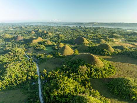 Aerial view of the Chocolate Hills with lush green conical mounds dense vegetation and a winding road in Batuan Central Visayas Philippines. Aerial view of the Chocolate Hills with lush green conical mounds dense vegetation and a winding road in Batuan Central Visayas Philippines.