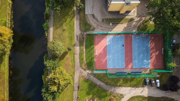 Aerial view of a vibrant sports court where blue and red hues meet amidst lush greenery adjacent to a tranquil canal Bydgoszcz Województwo kujawsko pomorskie Poland. Aerial view of a vibrant sports court where blue and red hues meet amidst lush greenery adjacent to a tranquil canal Bydgoszcz Województwo kujawsko pomorskie Poland.