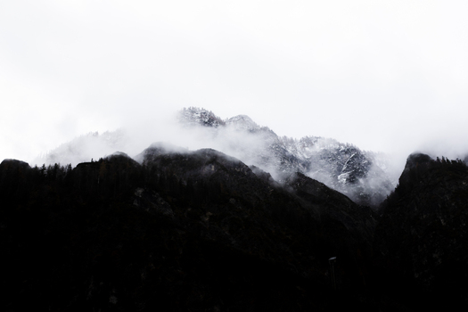 View of dark silhouetted mountain peaks partially shrouded in thick white fog and misty clouds Hallstatt Upper Austria Austria. View of dark silhouetted mountain peaks partially shrouded in thick white fog and misty clouds Hallstatt Upper Austria Austria.