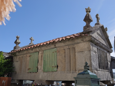 View of a traditional stone horreo granary with green wooden shutters and stone crosses on the roof in Combarro Pontevedra Spain.