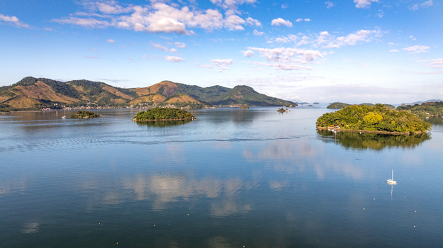 Aerial view of the islands and calm waters of Angra dos Reis featuring lush green hills a small sailboat and a clear blue sky in Angra dos Reis Rio de Janeiro Brazil.
