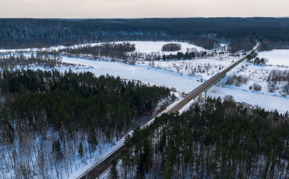 Aerial view of a bridge spanning a frozen river surrounded by snow covered evergreen forests and white fields Lithuania. Aerial view of a bridge spanning a frozen river surrounded by snow covered evergreen forests and white fields Lithuania.