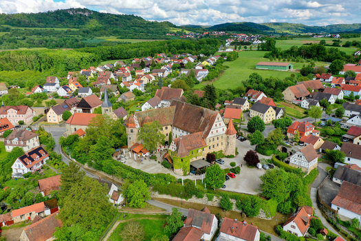 Wiesenthau Germany 02 May 2026 Aerial view of Schloss Wiesenthau with its historic stone walls and red tiled roofs surrounded by village houses and lush green hills. Wiesenthau Germany 02 May 2026 Aerial view of Schloss Wiesenthau with its historic stone walls and red tiled roofs surrounded by village houses and lush green hills.