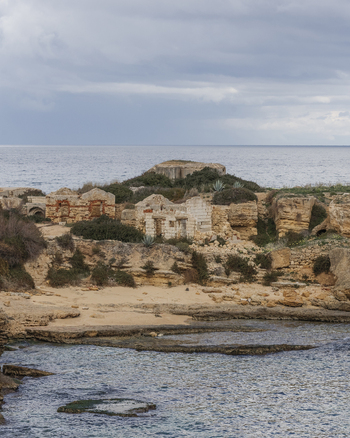 View of ancient stone ruins on a rocky coastline overlooking the Mediterranean Sea under a cloudy sky in Syracuse Sicily Italy.