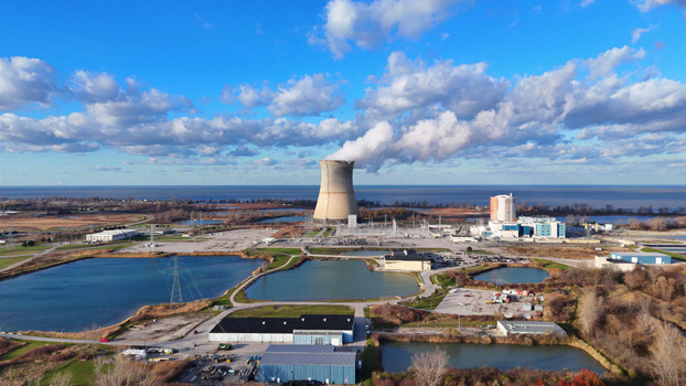 Aerial view of Davis Besse Nuclear Power Station with its cooling tower emitting steam surrounded by industrial facilities ponds and the Lake Erie shoreline in Oak Harbor Ohio United States.