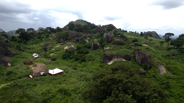 Aerial view of Idanre Hill featuring massive rock formations lush green vegetation and small rural dwellings under a cloudy sky in Idanre Ondo State Nigeria. Aerial view of Idanre Hill featuring massive rock formations lush green vegetation and small rural dwellings under a cloudy sky in Idanre Ondo State Nigeria.