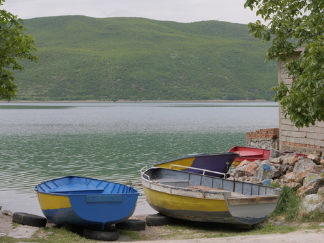 View of colorful small boats resting on the shore of Lake Ohrid with green hills in the background in Lin Korce County Albania.