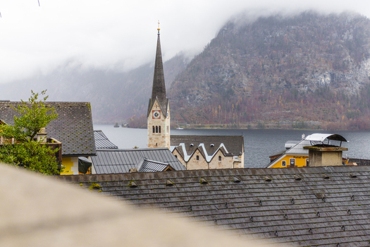 View of the Hallstatt Lutheran Church spire rising above traditional rooftops with the lake and misty mountains in the background Hallstatt Upper Austria Austria. View of the Hallstatt Lutheran Church spire rising above traditional rooftops with the lake and misty mountains in the background Hallstatt Upper Austria Austria.