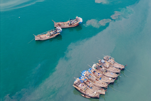 Moheskhali Upazila Bangladesh 11 March 2026 Aerial view of traditional wooden fishing boats with fishermen on board anchored in turquoise water. Moheskhali Upazila Bangladesh 11 March 2026 Aerial view of traditional wooden fishing boats with fishermen on board anchored in turquoise water.