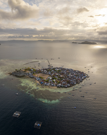 Aerial view of Pulau Mesa island village with dense houses wooden piers and fishing boats surrounded by turquoise waters in Kecamatan Komodo Nusa Tenggara Timur Indonesia. Aerial view of Pulau Mesa island village with dense houses wooden piers and fishing boats surrounded by turquoise waters in Kecamatan Komodo Nusa Tenggara Timur Indonesia.