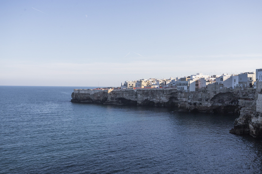 View of the iconic white houses perched on rugged limestone cliffs overlooking the calm Adriatic Sea in Polignano a Mare Apulia Italy.