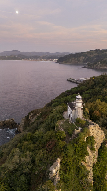 Aerial view of Getariako Itsasargia lighthouse perched on a rocky cliff overlooking the Bay of Biscay at sunset with lush greenery and coastal scenery in Getaria Euskadi Spain. Aerial view of Getariako Itsasargia lighthouse perched on a rocky cliff overlooking the Bay of Biscay at sunset with lush greenery and coastal scenery in Getaria Euskadi Spain.
