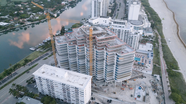 Aerial view of a high rise building under construction with a tall yellow crane situated between a canal and the sandy coastline in Miami Beach Florida United States. Aerial view of a high rise building under construction with a tall yellow crane situated between a canal and the sandy coastline in Miami Beach Florida United States.