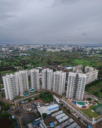 Aerial view of Puneville residential complex featuring modern high rise towers swimming pools and surrounding green fields in Pimpri Chinchwad Maharashtra India.