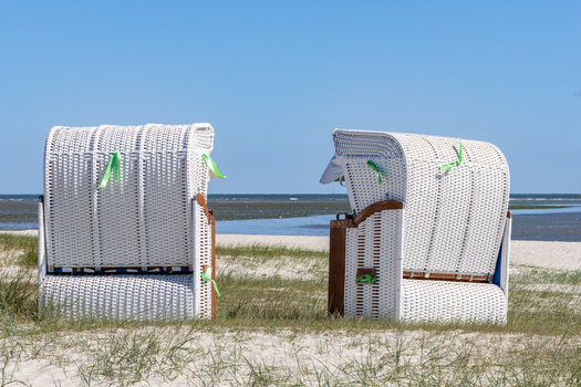 View of two white wicker beach chairs on the sandy dunes of Strand Schillig overlooking the North Sea under a clear blue sky in Wangerland Niedersachsen Germany. View of two white wicker beach chairs on the sandy dunes of Strand Schillig overlooking the North Sea under a clear blue sky in Wangerland Niedersachsen Germany.