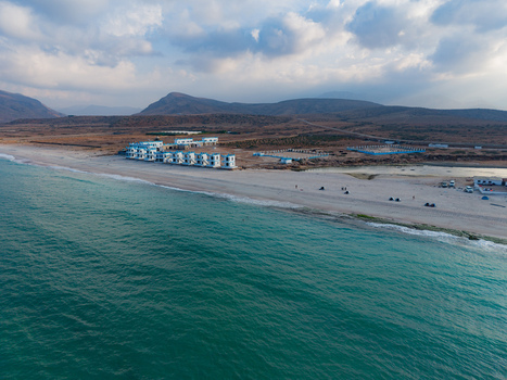 Aerial view of white buildings nestled along the sandy beach where turquoise waters meet the shore under a vast sky Ararhin Socotra Yemen. Aerial view of white buildings nestled along the sandy beach where turquoise waters meet the shore under a vast sky Ararhin Socotra Yemen.