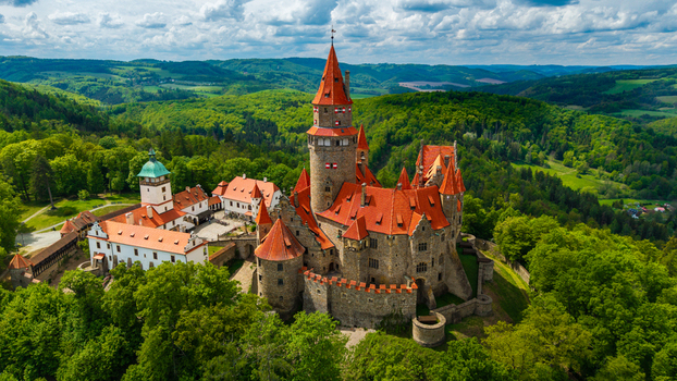 Aerial view of Bouzov Castle with its iconic red tiled roofs and tall central tower nestled among lush green forests under a cloudy sky Bouzov Olomoucky kraj Czechia. Aerial view of Bouzov Castle with its iconic red tiled roofs and tall central tower nestled among lush green forests under a cloudy sky Bouzov Olomoucky kraj Czechia.