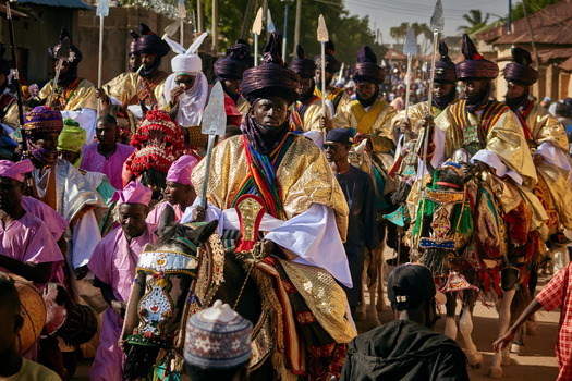 Zaria city Nigeria 22 March 2026 View of a vibrant procession of richly adorned horsemen in gold and indigo robes moving through sun drenched streets watched by a lively crowd. Zaria city Nigeria 22 March 2026 View of a vibrant procession of richly adorned horsemen in gold and indigo robes moving through sun drenched streets watched by a lively crowd.