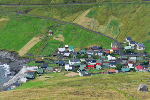 View of a small village with colorful houses nestled in a green valley along the rocky coastline of the Faroe Islands. View of a small village with colorful houses nestled in a green valley along the rocky coastline of the Faroe Islands.
