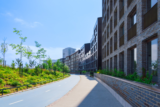 View of modern curved brick apartment buildings lining a paved path with green landscaping under a clear blue sky in Helsinki Uusimaa Finland.