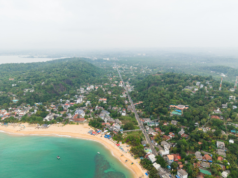 Aerial view of Unawatuna Beach with turquoise water and coastal buildings nestled among lush tropical greenery in Unawatuna Southern Province Sri Lanka.