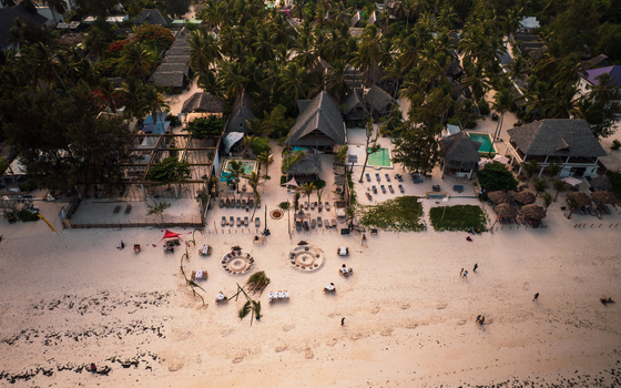Aerial view of soft sandy beach meeting the turquoise ocean fringed by verdant palms and quaint thatch roofed structures Paje Unguja South Region Tanzania. Aerial view of soft sandy beach meeting the turquoise ocean fringed by verdant palms and quaint thatch roofed structures Paje Unguja South Region Tanzania.