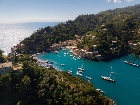 Aerial view of the iconic harbor with luxury yachts and colorful houses nestled against lush green hills in Portofino Liguria Italy.