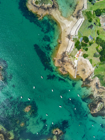 Aerial view of the turquoise waters surrounding the island of Brehat featuring small boats anchored in the bay sandy beaches and rocky coastline in Ile de Brehat Brittany France.