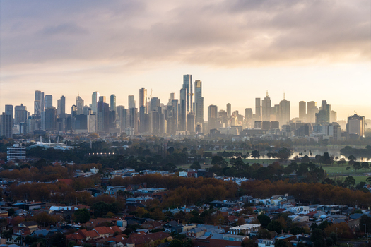 Aerial view of the Melbourne city skyline featuring modern skyscrapers rising above urban residential areas and Albert Park under a soft golden hour sky in Melbourne Victoria Australia. Aerial view of the Melbourne city skyline featuring modern skyscrapers rising above urban residential areas and Albert Park under a soft golden hour sky in Melbourne Victoria Australia.